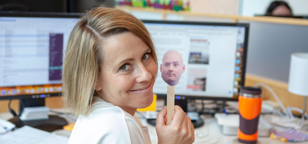 A photo of Erin holding up an image of Charlie's head on a popscicle stick